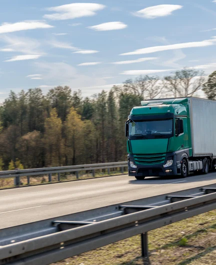 889a568d-09a2-43cf-b604-fb486147005c-green-semi-truck-with-white-trailer-driving-highway-vehicle-moves-along-road.jpg